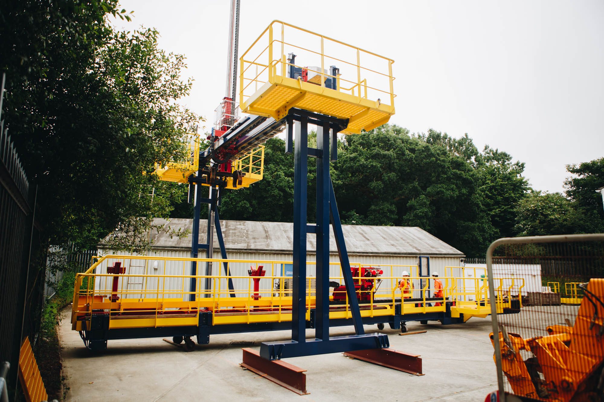 Yellow access platform raised on a blue mast above a wheeled deck structure in a test yard