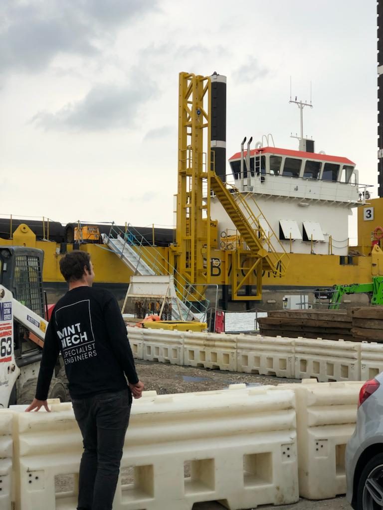 MintMech engineer looking across a quayside towards a workboat with a yellow mast