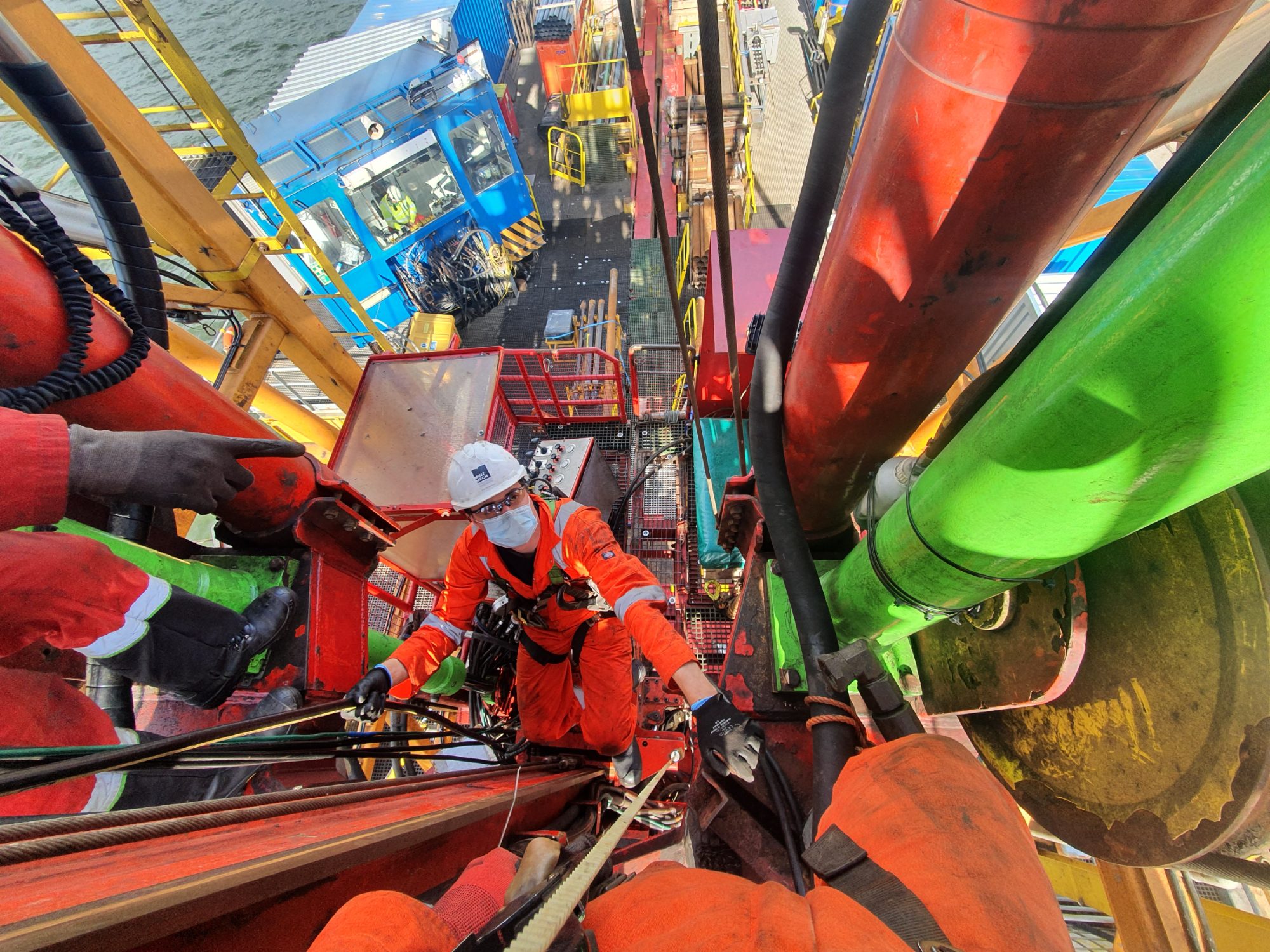 Engineer in orange coveralls working among large-diameter drill pipe, seen from above