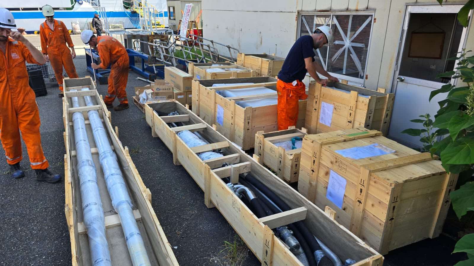Engineers checking drilling equipment packed in timber crates on a quayside