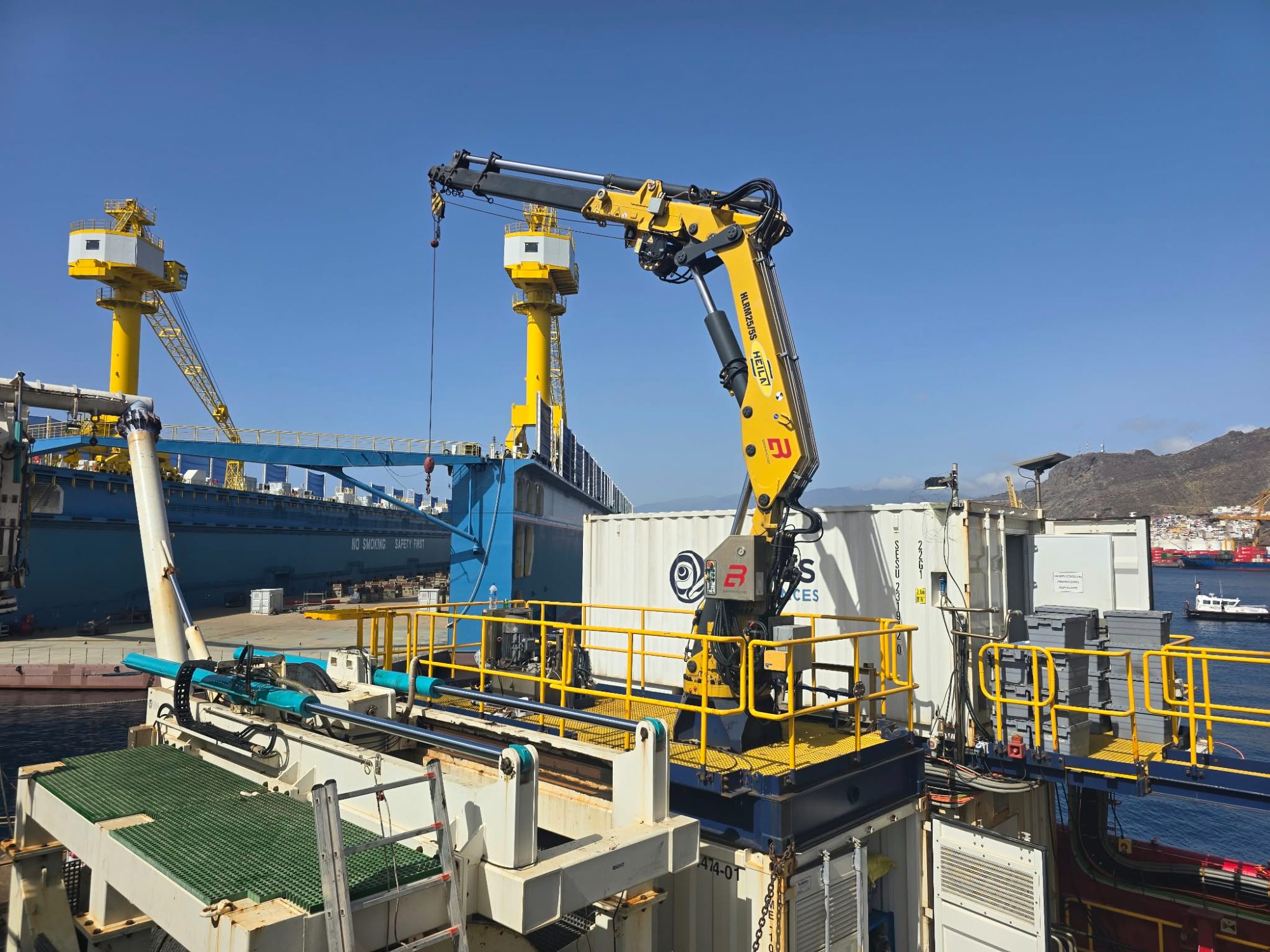 Yellow knuckle-boom crane mounted on a container on a vessel deck