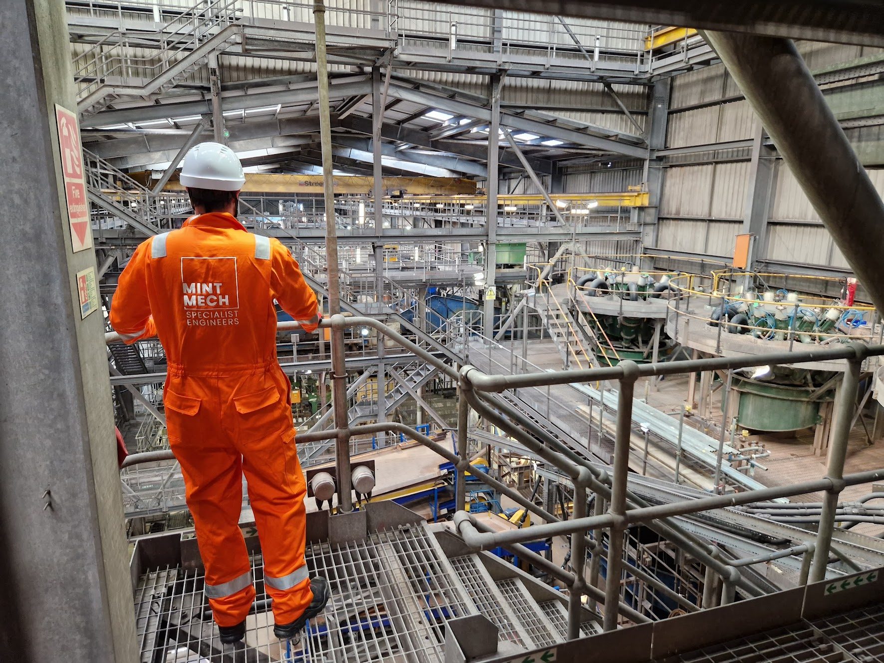 MintMech engineer in orange coveralls looking out over a mineral processing plant
