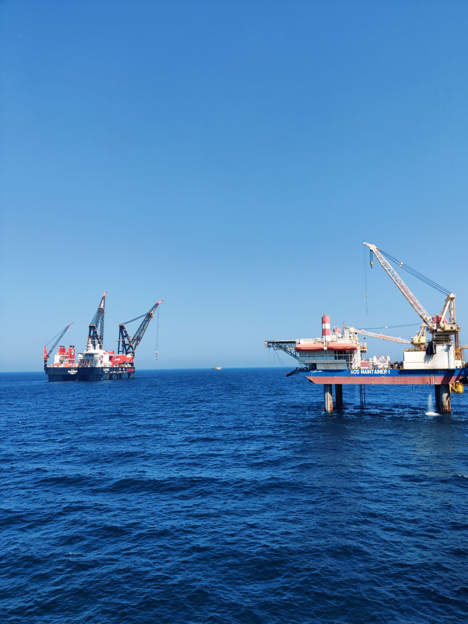 Heavy-lift crane vessel and a jack-up platform working offshore under a clear sky