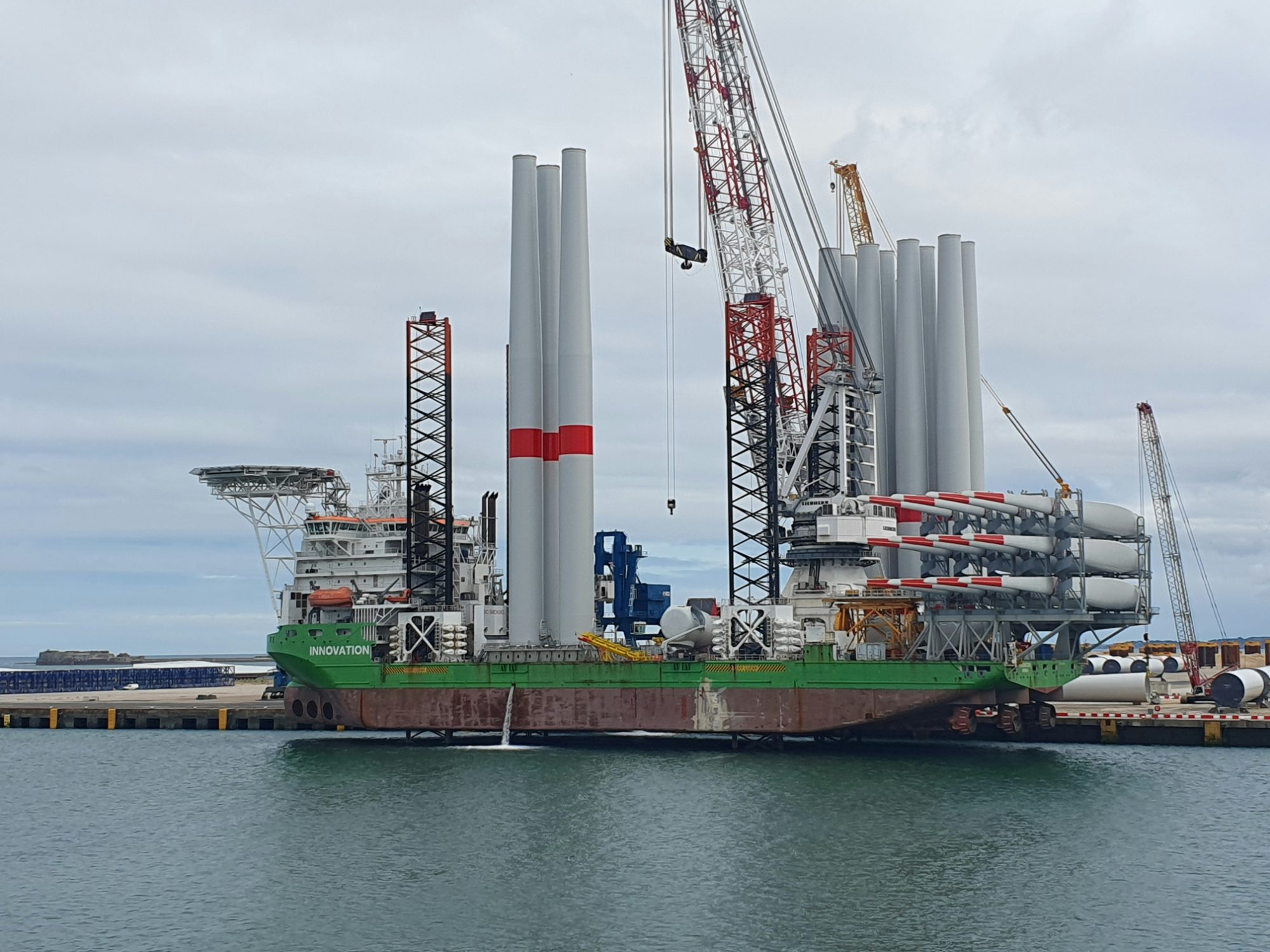 Jack-up installation vessel loaded with wind turbine towers and blades alongside a quay