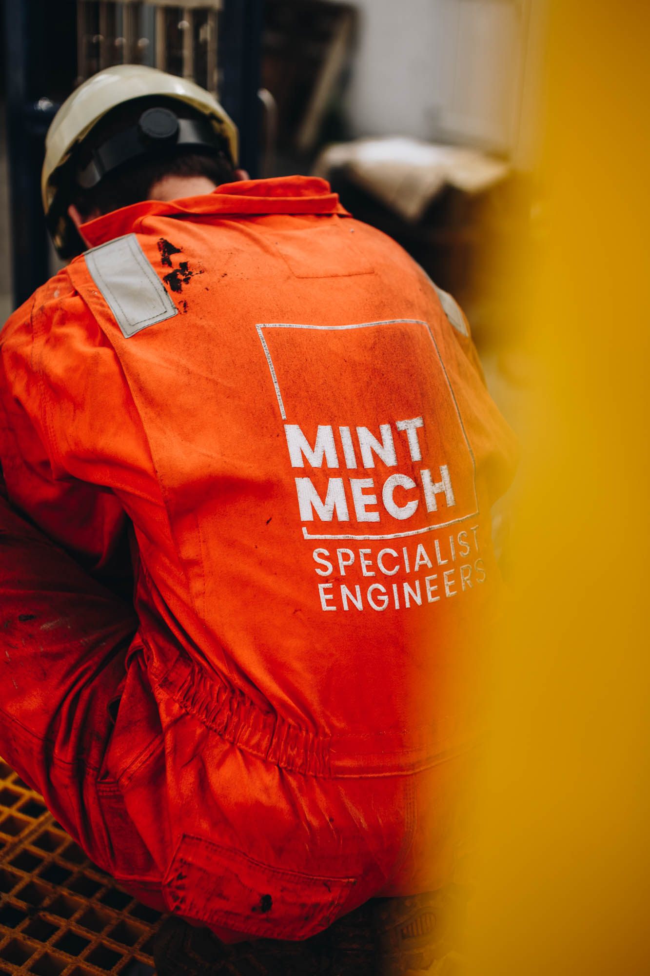 Engineer in orange MintMech coveralls and a hard hat, seen from behind