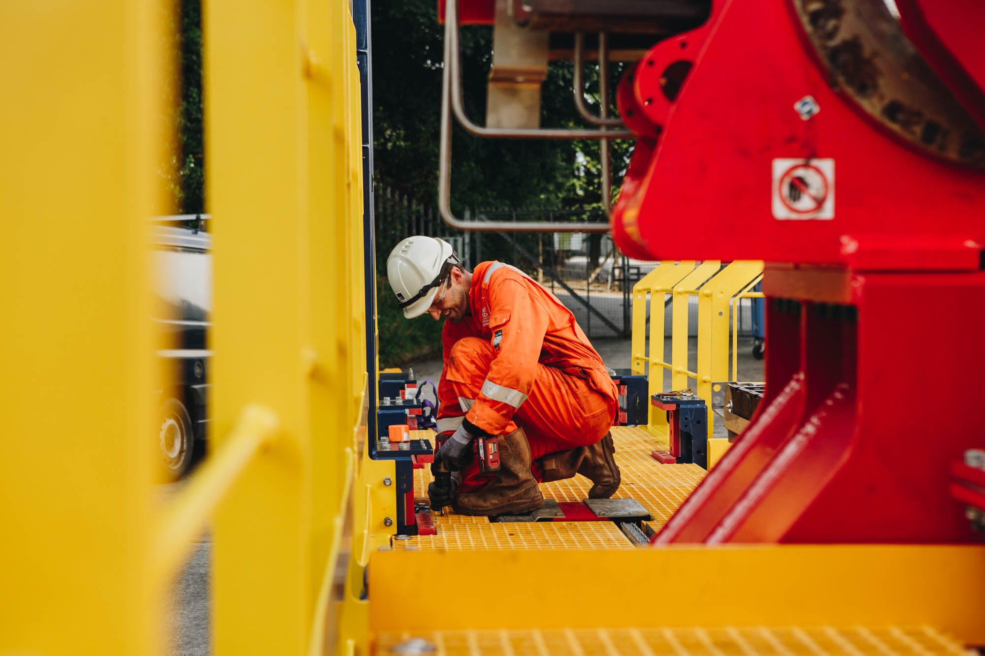 Engineer in orange coveralls and a hard hat working on yellow and red deck equipment