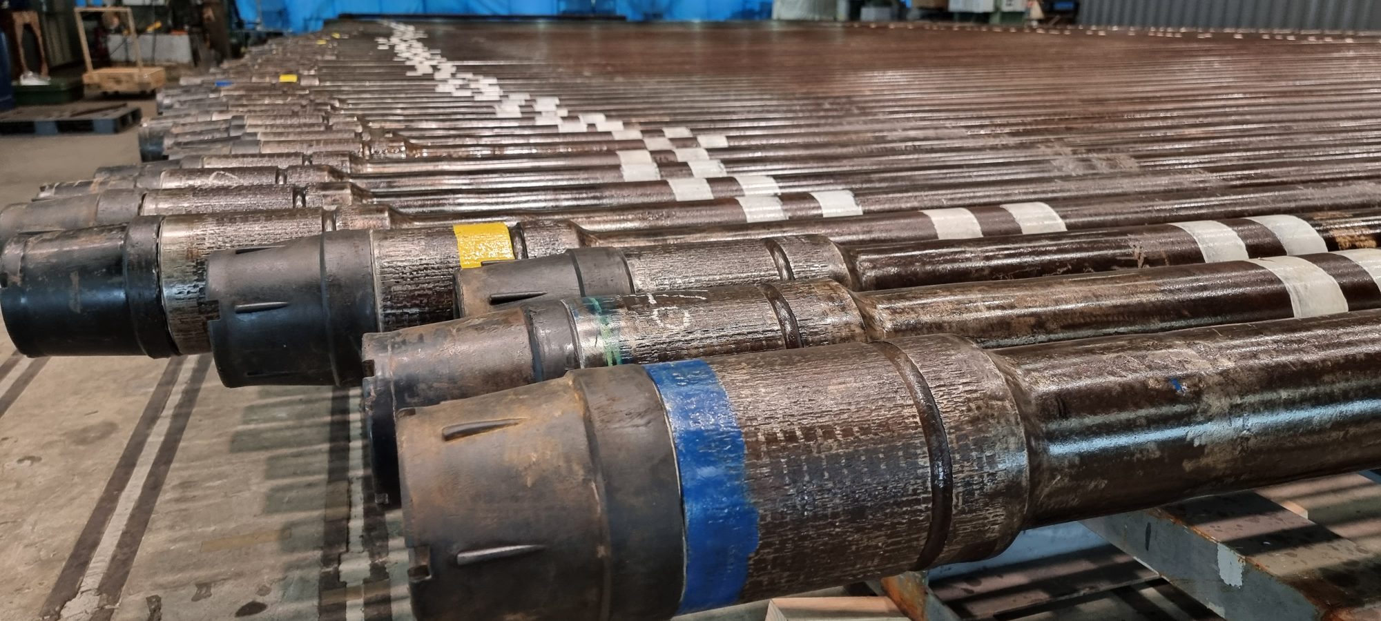 Rows of drill pipe laid out on racks in a workshop
