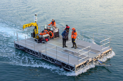 Three people on a small aluminium work pontoon under way on the water