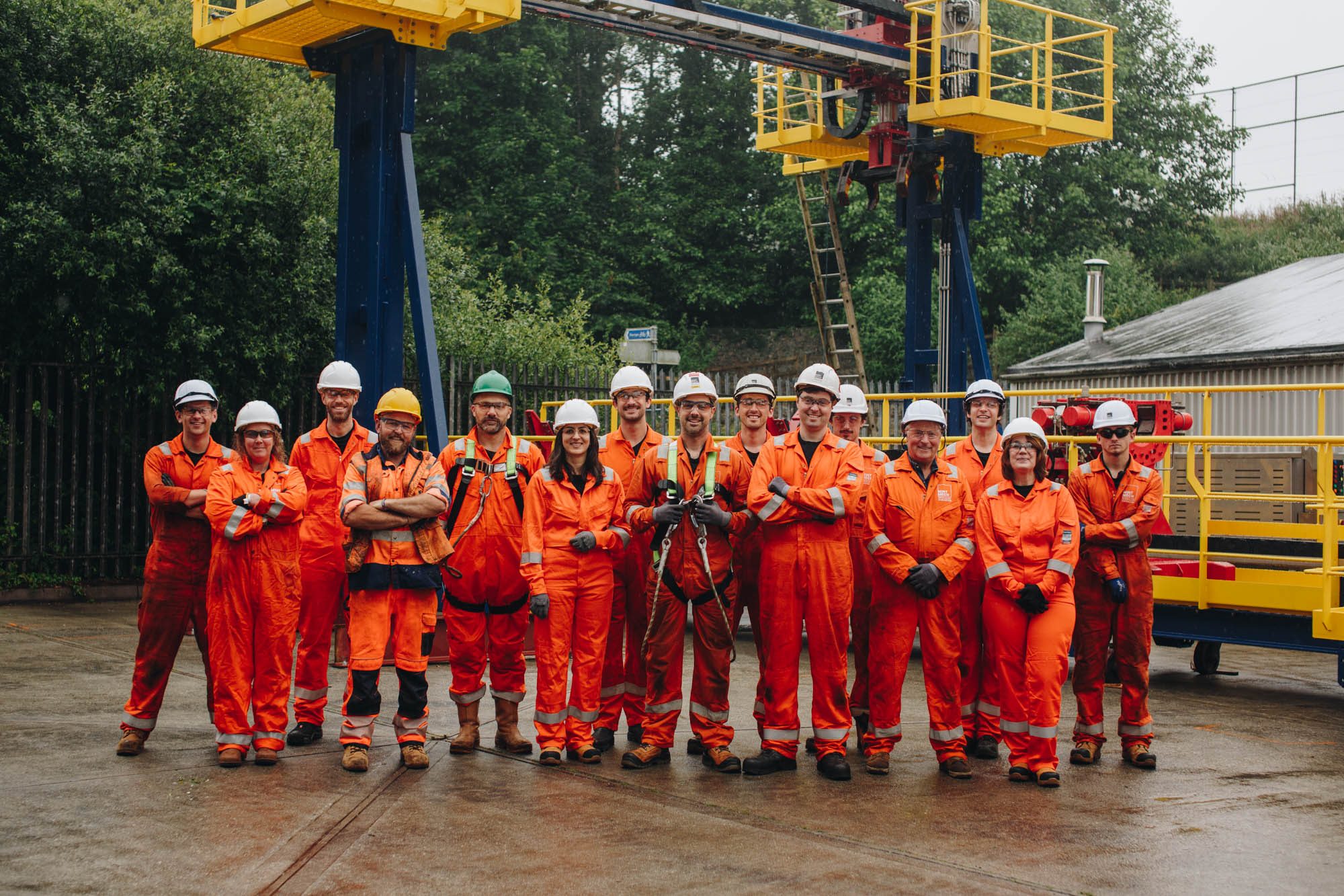 The MintMech team in orange coveralls and hard hats in front of a yellow access platform