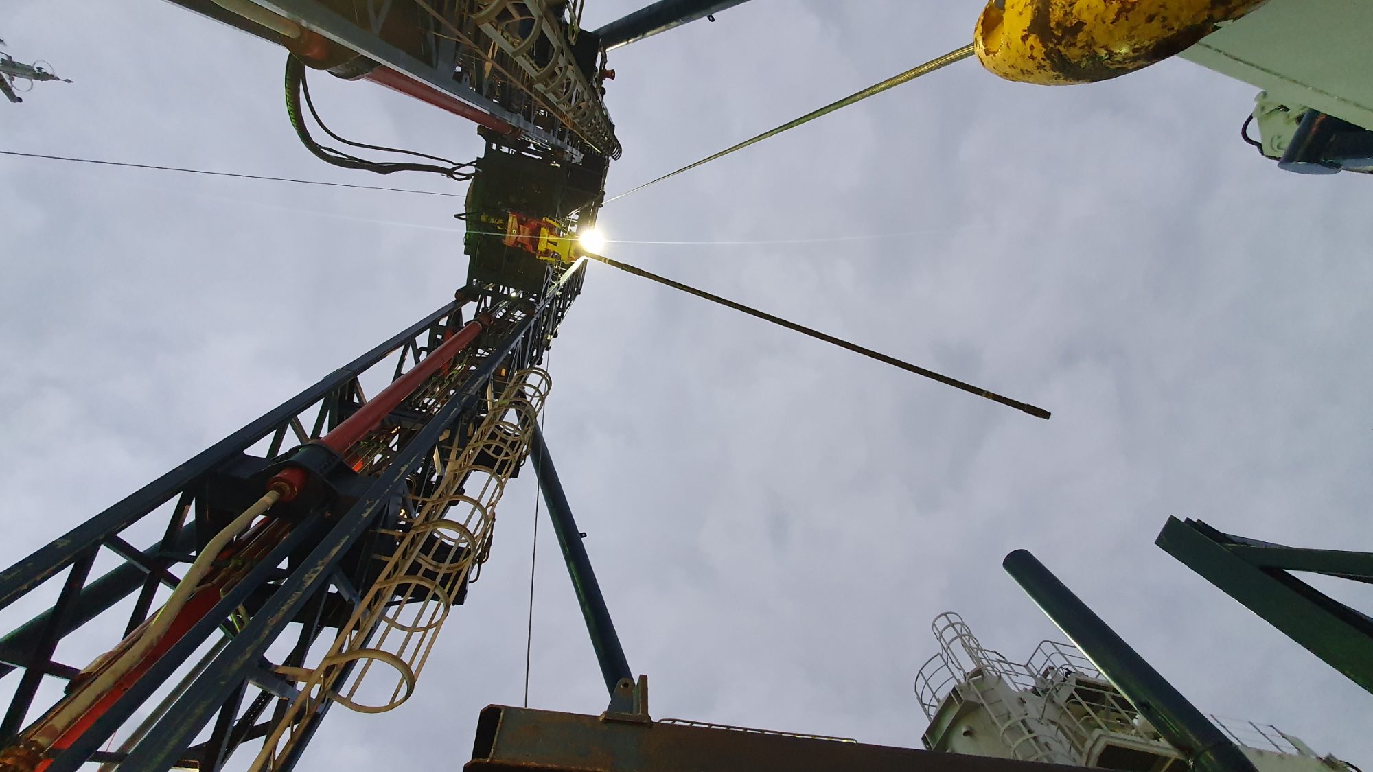 Looking up a geotechnical drilling mast against a bright sky