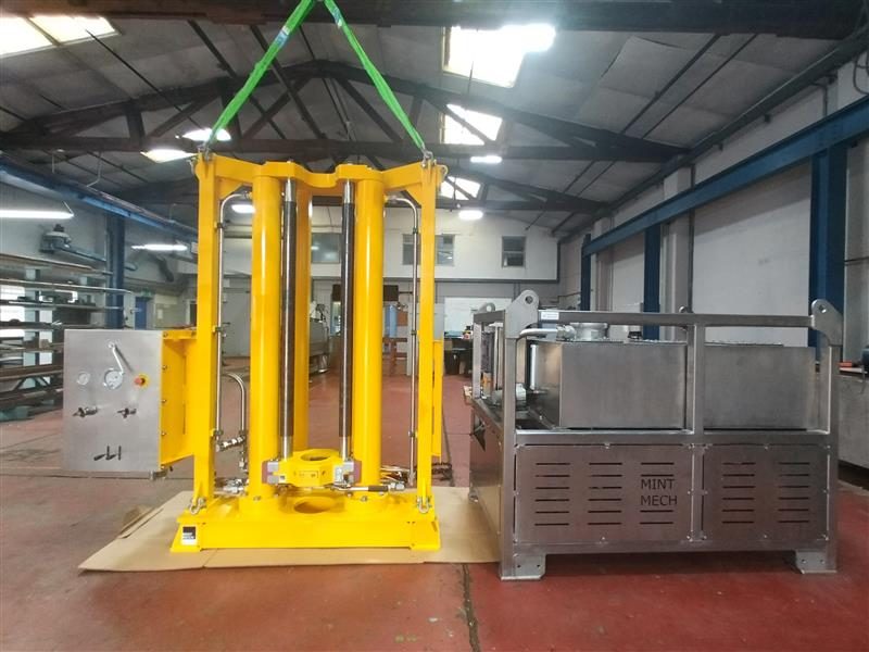 Yellow seabed frame lifted on a sling beside a stainless steel control cabinet in a workshop