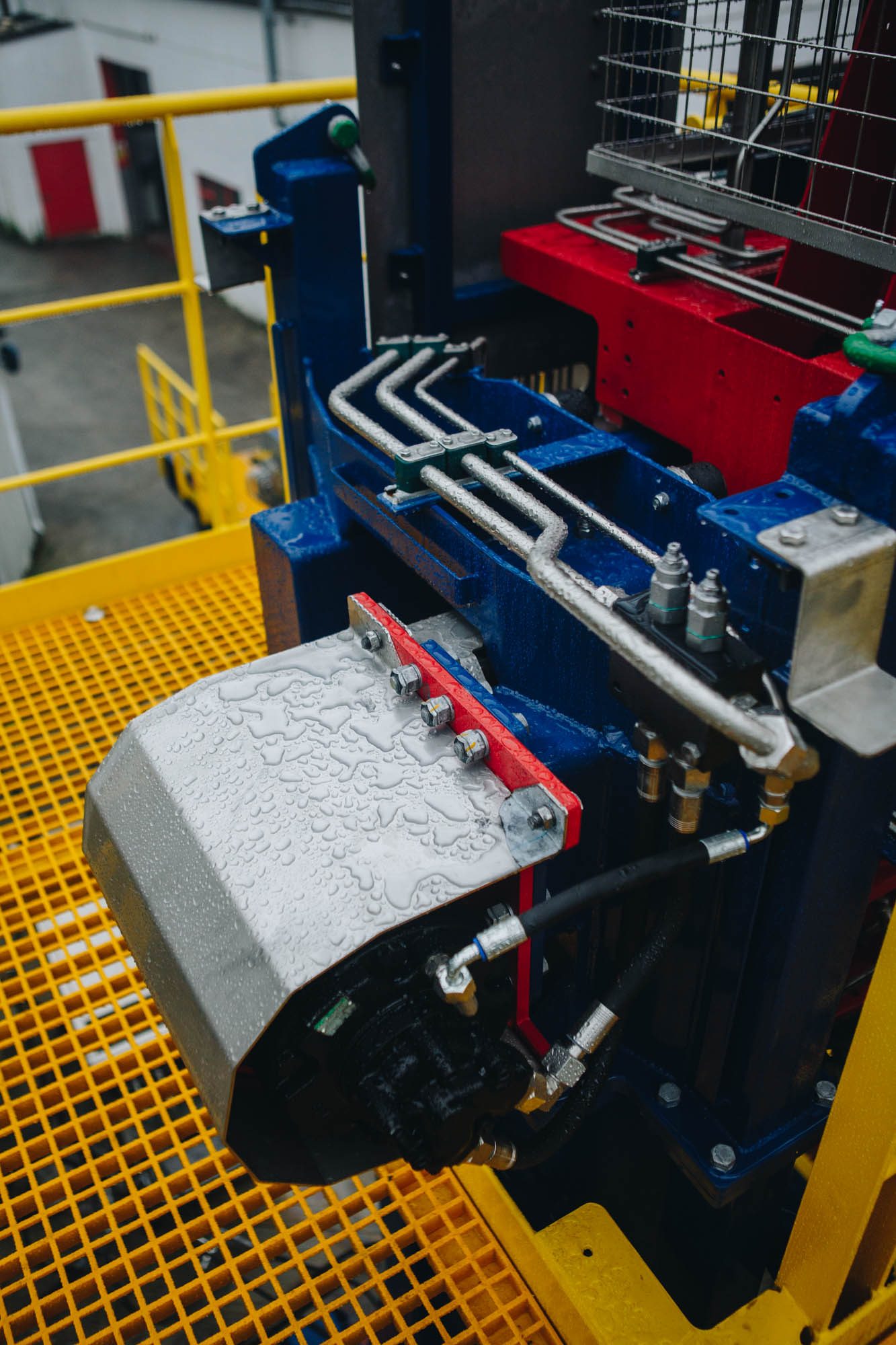 Hydraulic drive unit and pipework on blue equipment above a yellow grating walkway