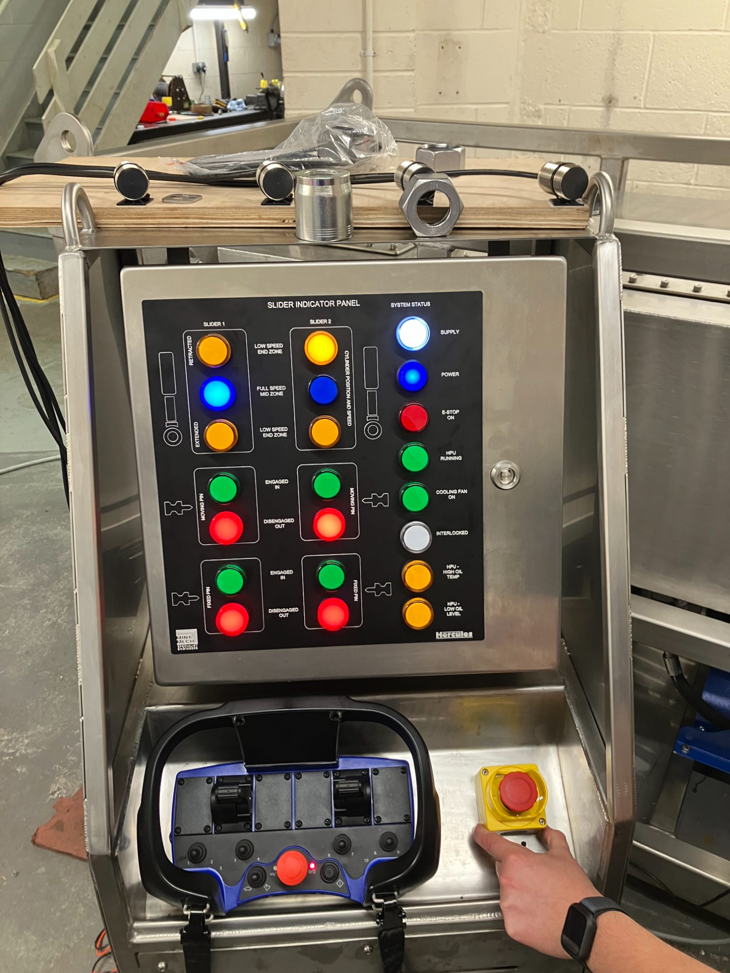 Operator at a stainless steel control station with indicator lamps and a handheld remote