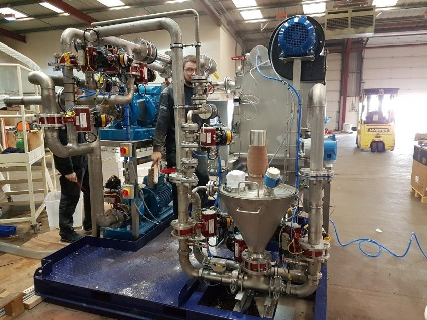 Mud mixing skid with a stainless steel hopper, pumps and pipework in a workshop