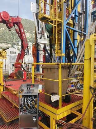 Control stand with hydraulic hoses on a drilling deck beside a red crane