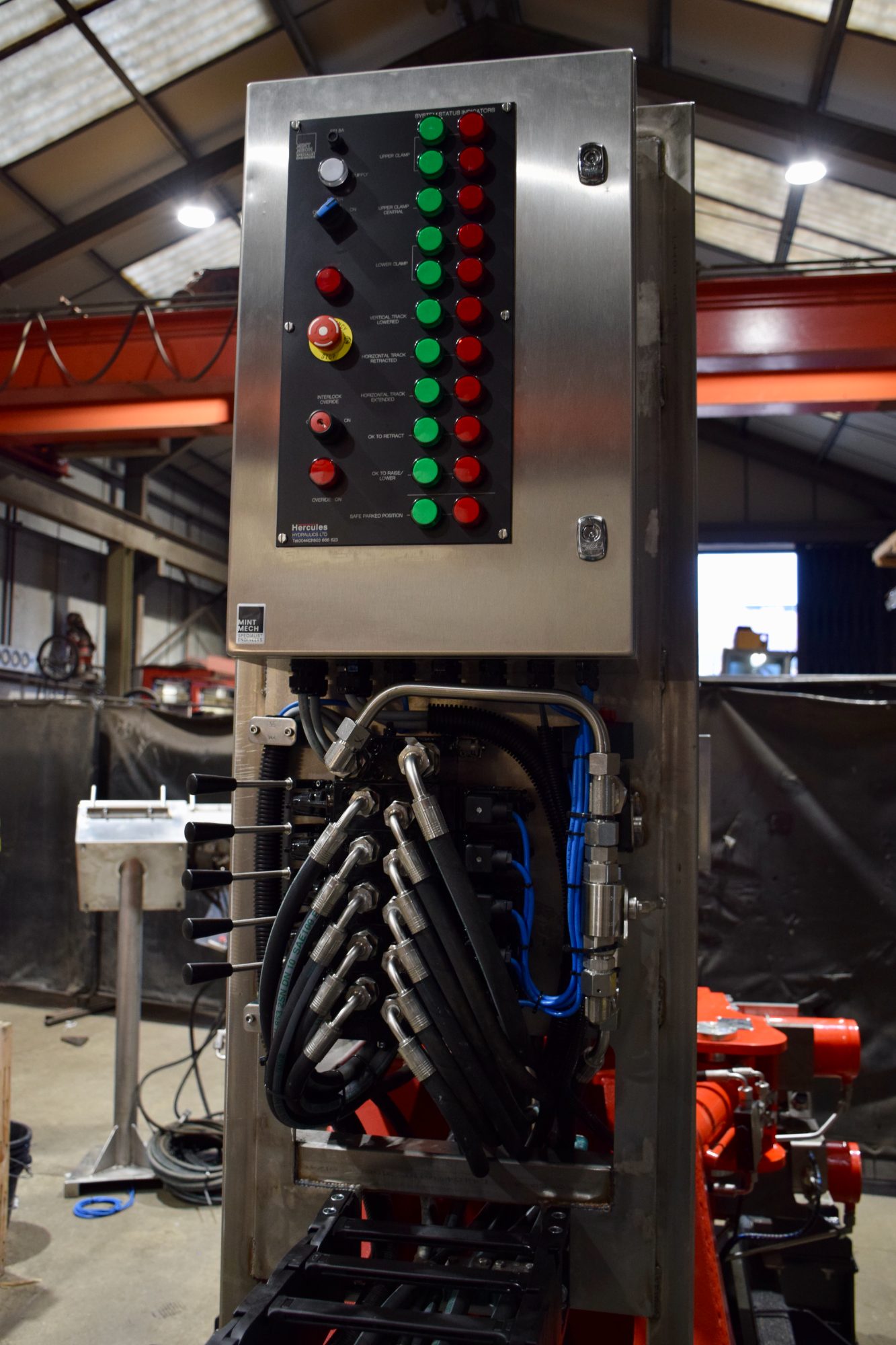 Stainless steel control panel with rows of indicator lamps above hydraulic hose connections