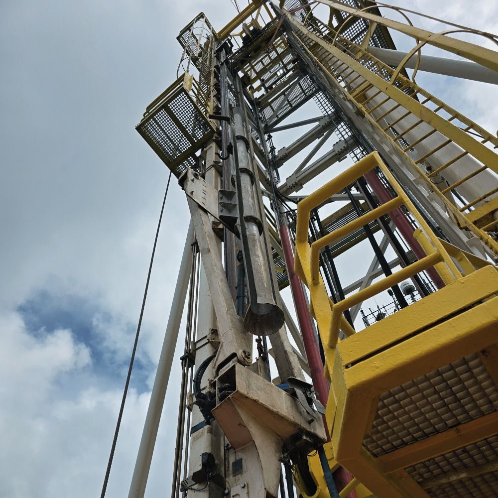 Looking up a drilling mast at a tool handler arm beside a yellow work platform