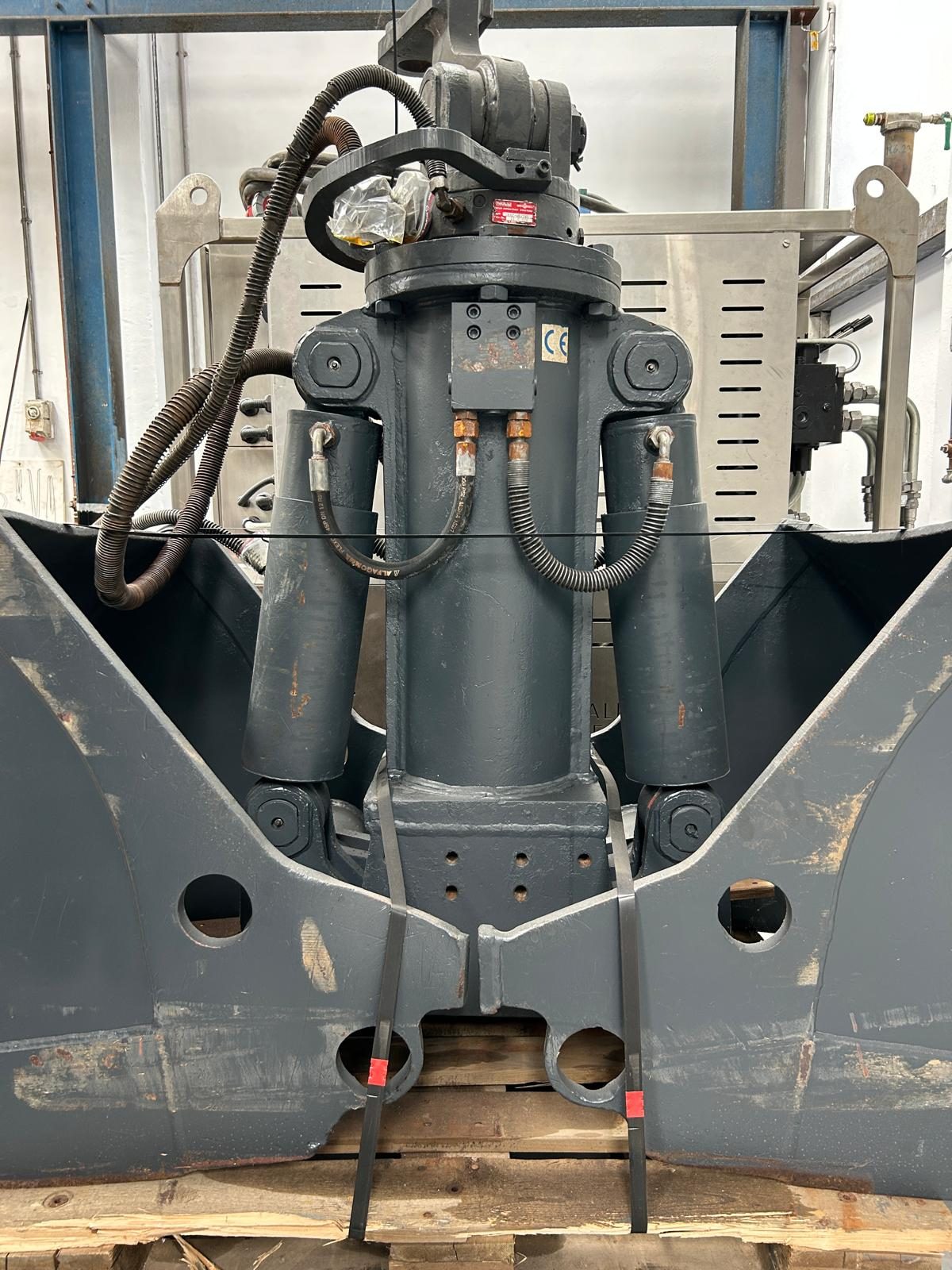 Hydraulic clamshell grab with its cylinders and hoses, standing in a workshop