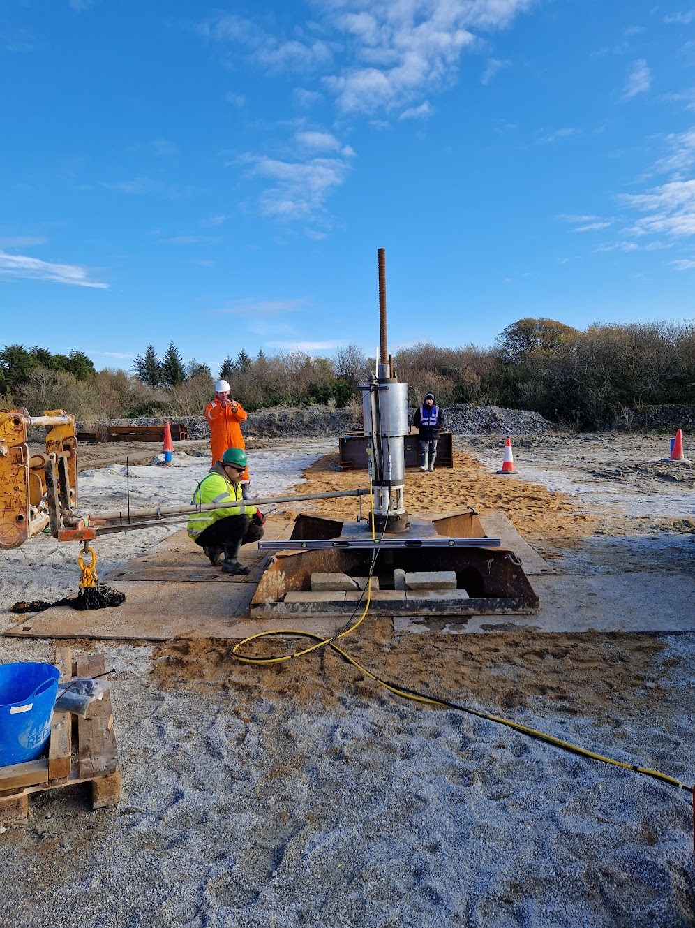 Drilling equipment set up on a base frame on open ground, with engineers alongside