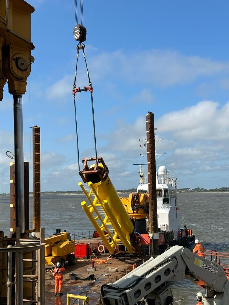 Crane lowering a yellow frame onto a jack-up barge deck beside a workboat