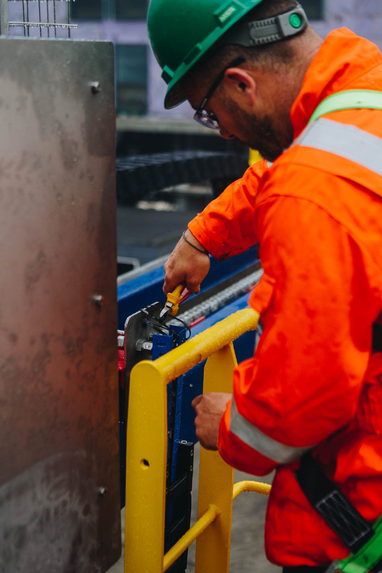 Engineer in a green hard hat tightening a fitting on a yellow handrail