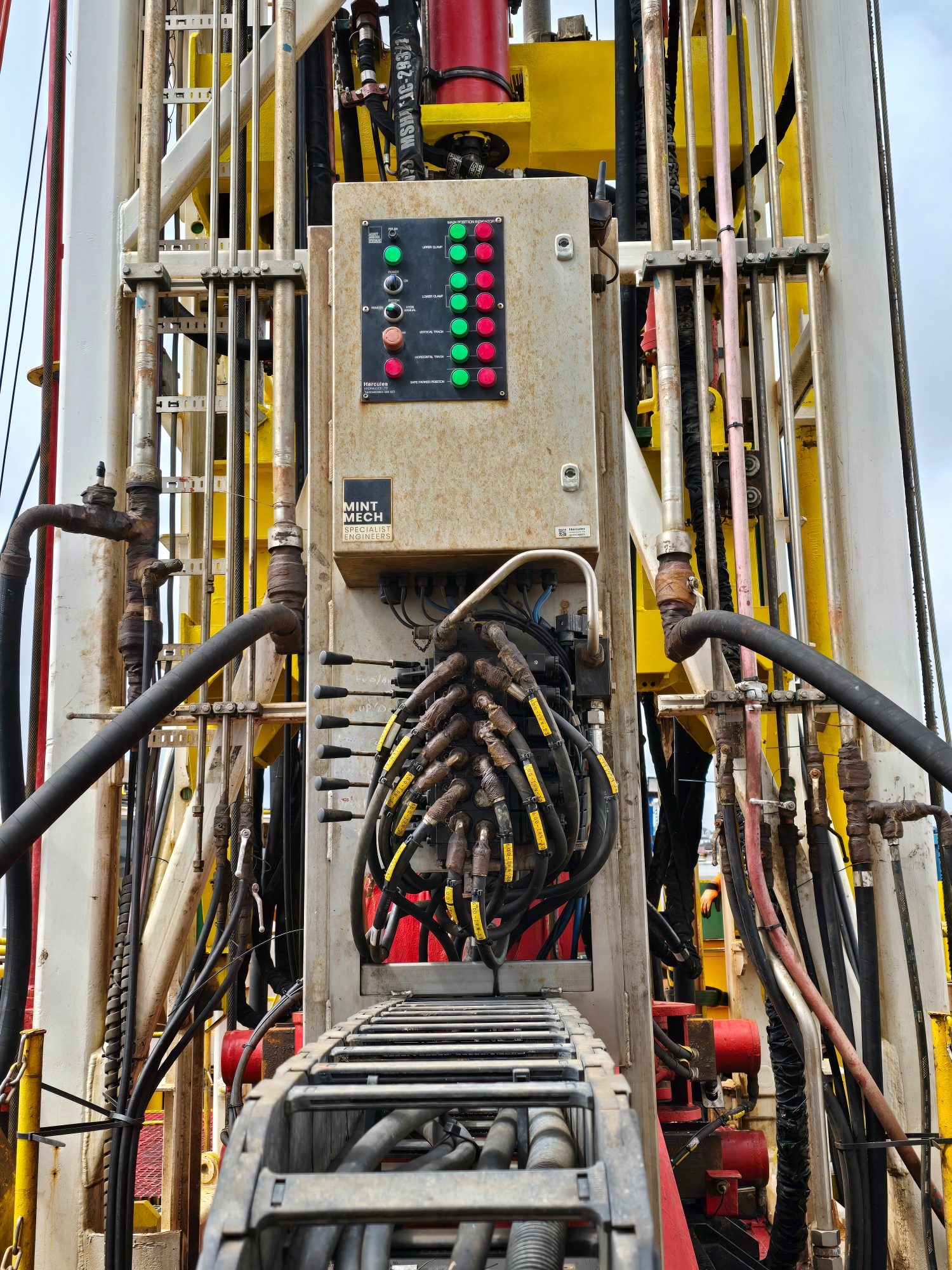 Control box with indicator lamps and bundled hydraulic hoses fitted to a drilling mast