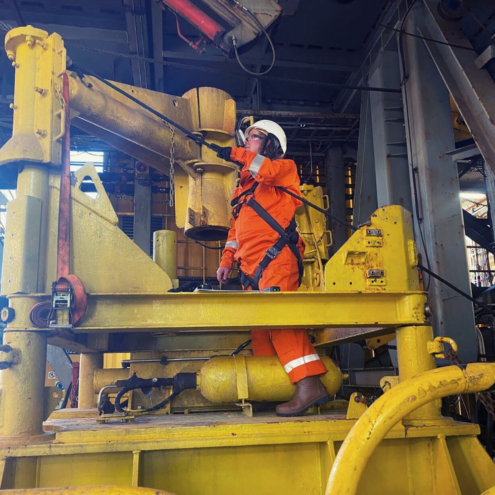 Engineer in orange coveralls and a harness working on a yellow seabed frame