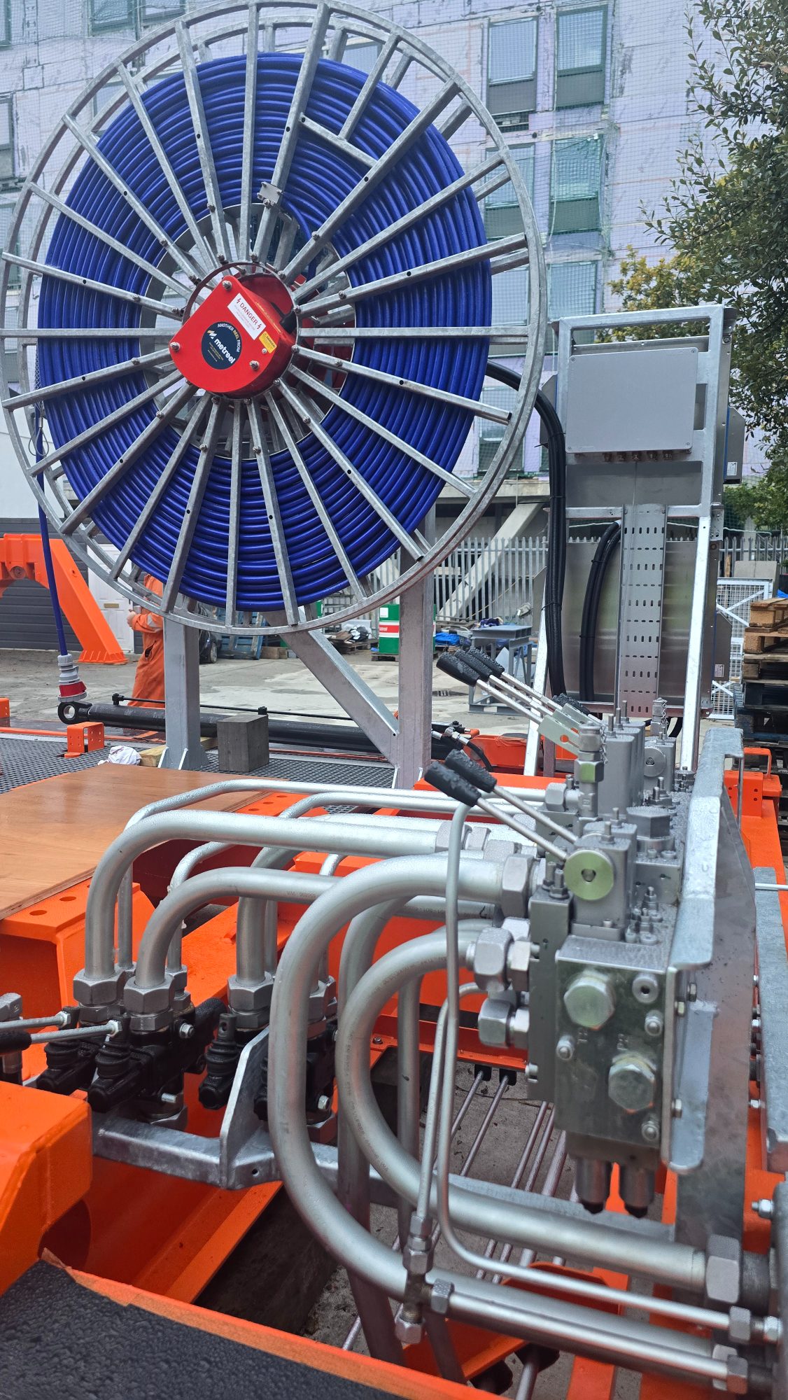 Blue hose reel above a bank of hydraulic valves and steel pipework on an orange frame