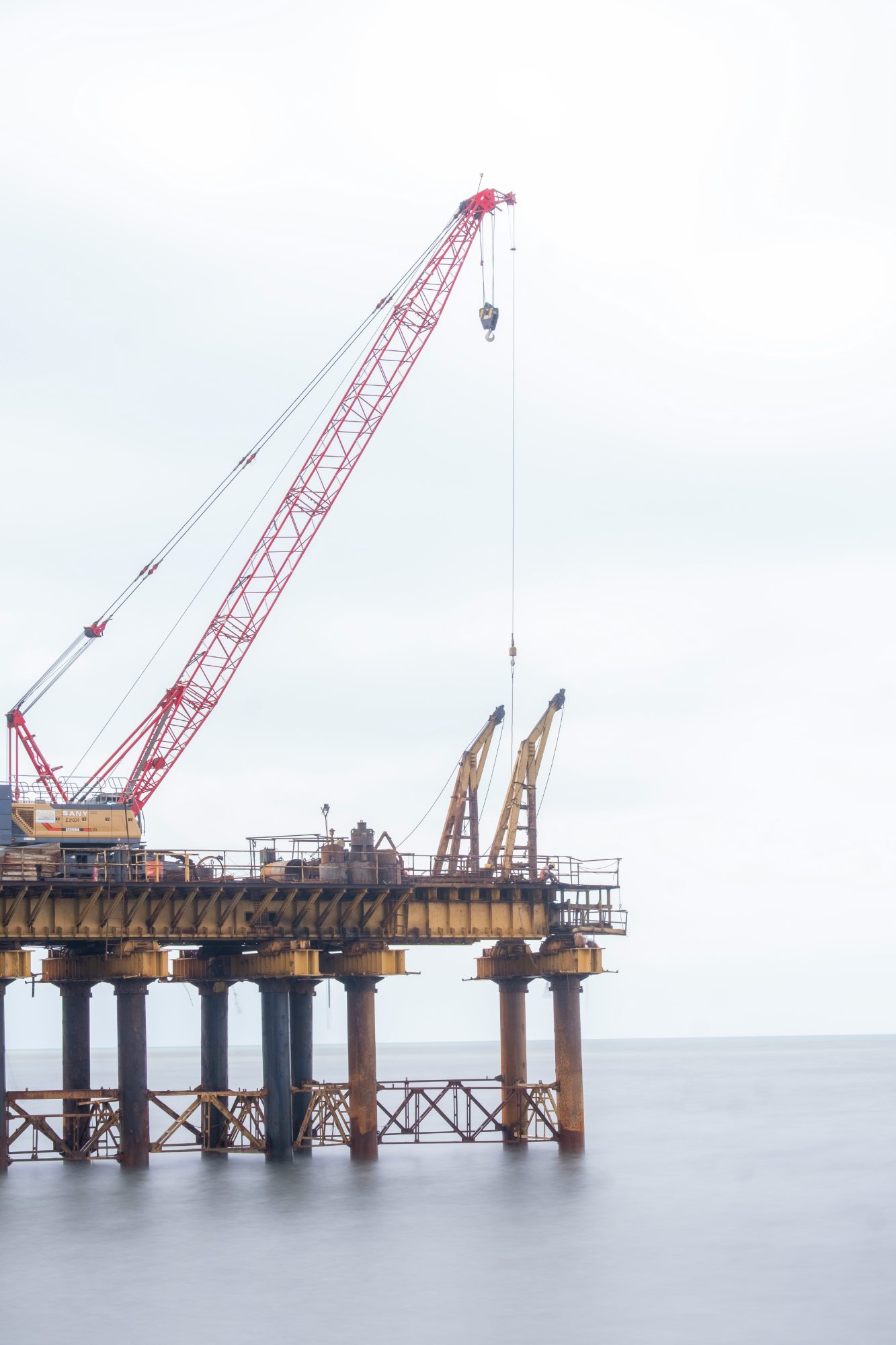 Crane working from a jetty platform on piles over a calm, misty sea