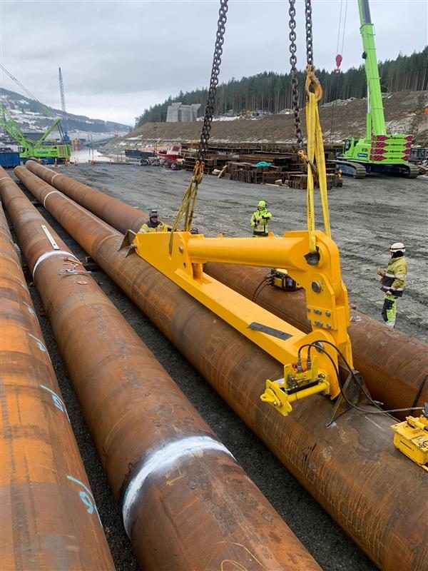 Yellow lifting tool being lowered onto steel tubular piles on a quayside