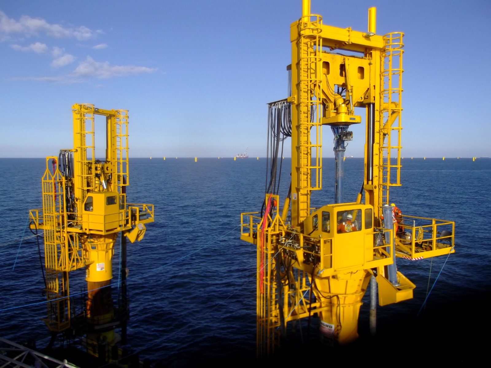Two yellow pile-top drilling rigs mounted on piles at sea