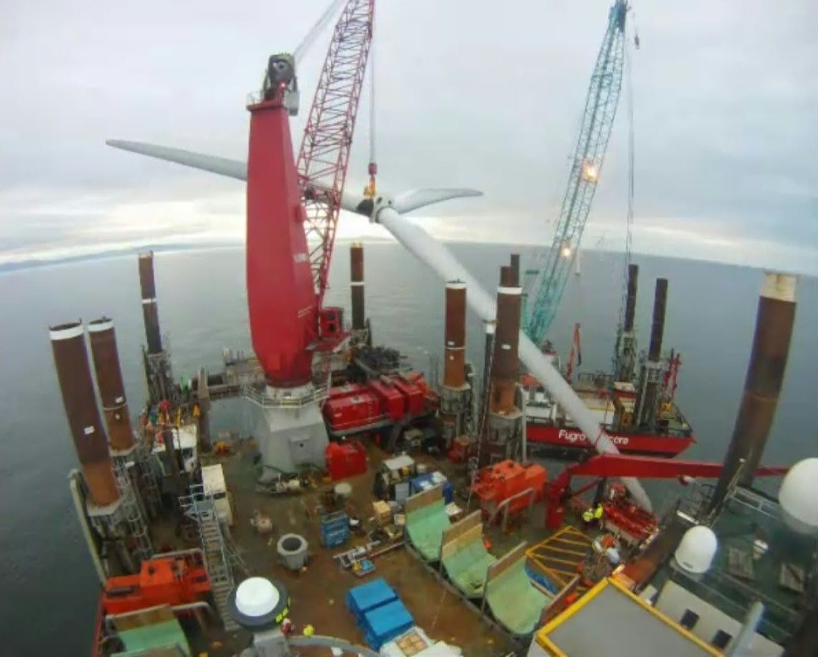 Wide-angle view down onto a jack-up vessel's deck beside an offshore wind turbine
