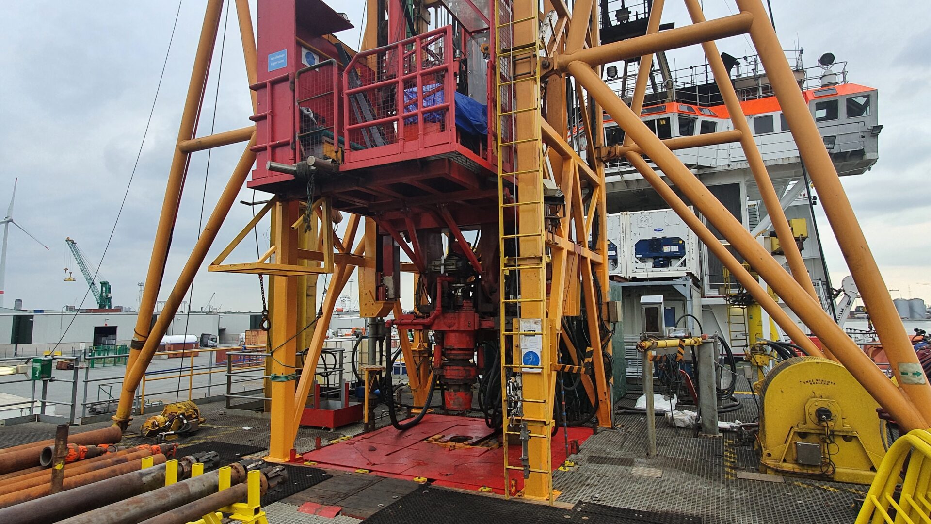 View of the base of a drill derrick from the deck. Several elements of the marine deck spread are visible